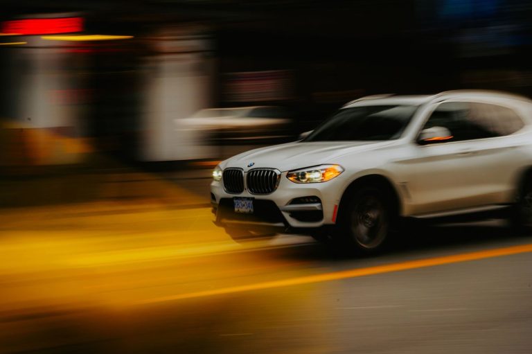 SUV branco da BMW em movimento por uma rua urbana, com efeito de desfoque.