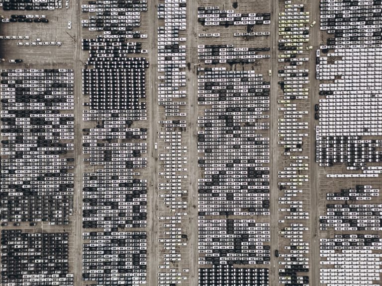 Vista aérea de um amplo pátio repleto de veículos novos no Brasil.